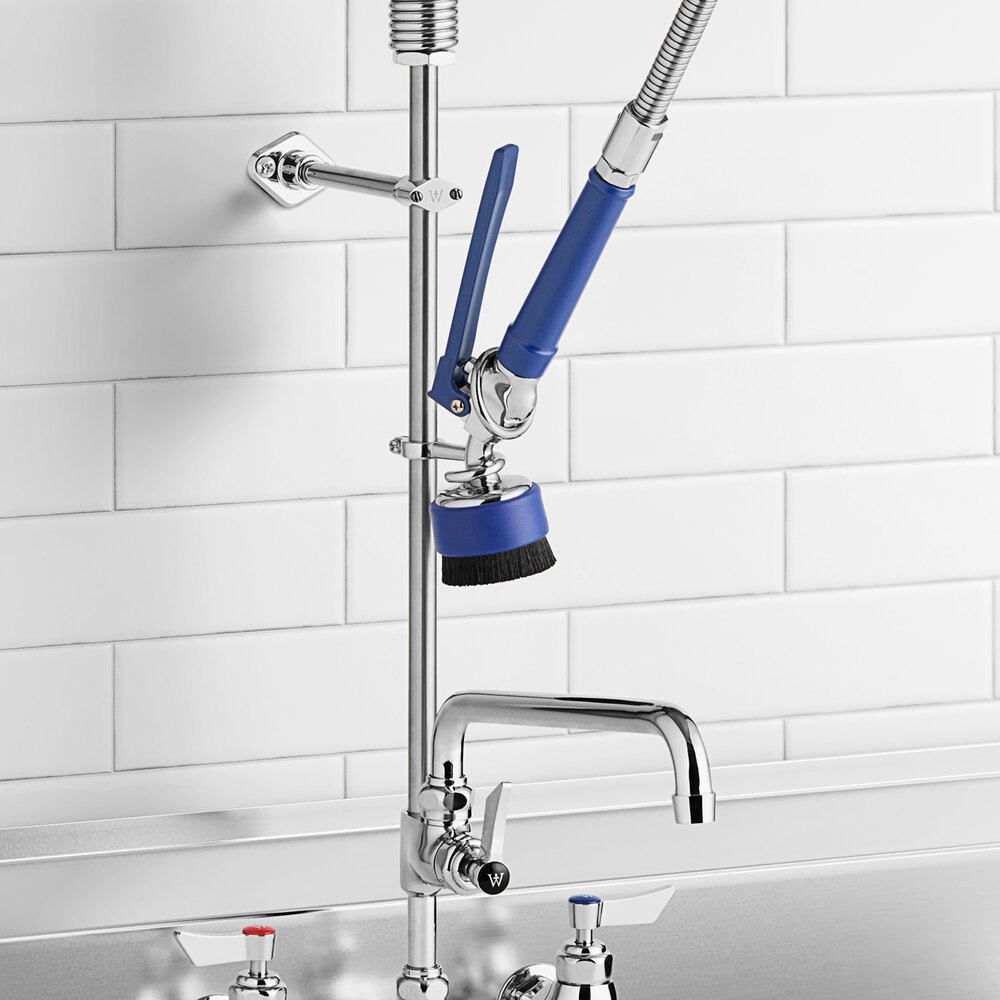 A commercial sink faucet with an attached blue-handled black nylon scrub brush.